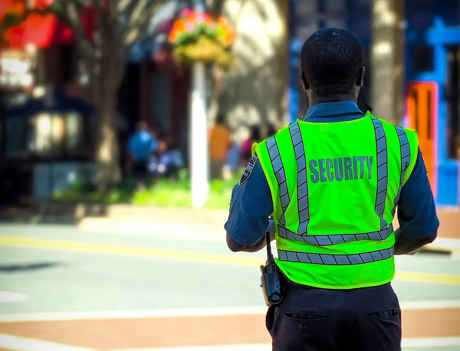 man facing away from the camera with a bright yellow security vest on and a walkie talkie on his hip